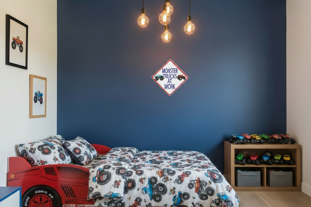 Monster truck street sign wall decal on navy blue accent wall in a boys bedroom — 12x12 inch peel and stick vinyl decal with framed monster truck art prints on surrounding walls, wood shelf with monster truck toys